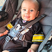 Helios is registered to the contest to win money with this photo: baby, child, car_seat, seatbelt, black_jersey, yellow_stripes, smiling, tongue_out, happy, infant, closeup, person, cute, casual, indoor, portrait, strapped_in, clothing, safety, seat