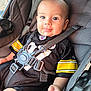 baby, child, car_seat, seatbelt, black_jersey, yellow_stripes, smiling, tongue_out, happy, infant, closeup, person, cute, casual, indoor, portrait, strapped_in, clothing, safety, seat