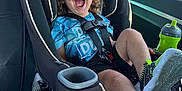 Caspian is registered to the contest to win money with this photo: child, toddler, car_seat, seat_belt, smiling, laughing, curly_hair, sippy_cup, green_shoes, sneakers, car_interior, window, sunshine, road_trip, travel, cup_holder, rear_seat, safety, candid, joyful