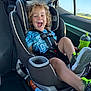 child, toddler, car_seat, seat_belt, smiling, laughing, curly_hair, sippy_cup, green_shoes, sneakers, car_interior, window, sunshine, road_trip, travel, cup_holder, rear_seat, safety, candid, joyful