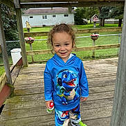 Caspian joined the competition — help win amazing prizes! child, toddler, smile, curly_hair, blue_hoodie, dinosaur_graphic, matching_pants, green_sneakers, sneakers, wooden_deck, porch, backyard, chain_link_fence, birdhouse, flower_pot, grass, trees, daylight, portrait, playful