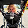 Caspian is registered to the contest to win money with this photo: child, smiling, curly_hair, stroller, canopy, wheels, mesh, hand, outdoors, sunlight, road, pavement, barcode_tag, joy, portrait, candid, park, stroller_handle, tire, shadow