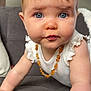 baby, child, crawling, blue_eyes, necklace, amber, white_clothing, indoor, couch, furniture, close_up, face, skin, hair, arm, person, curious, expression, infant, cute