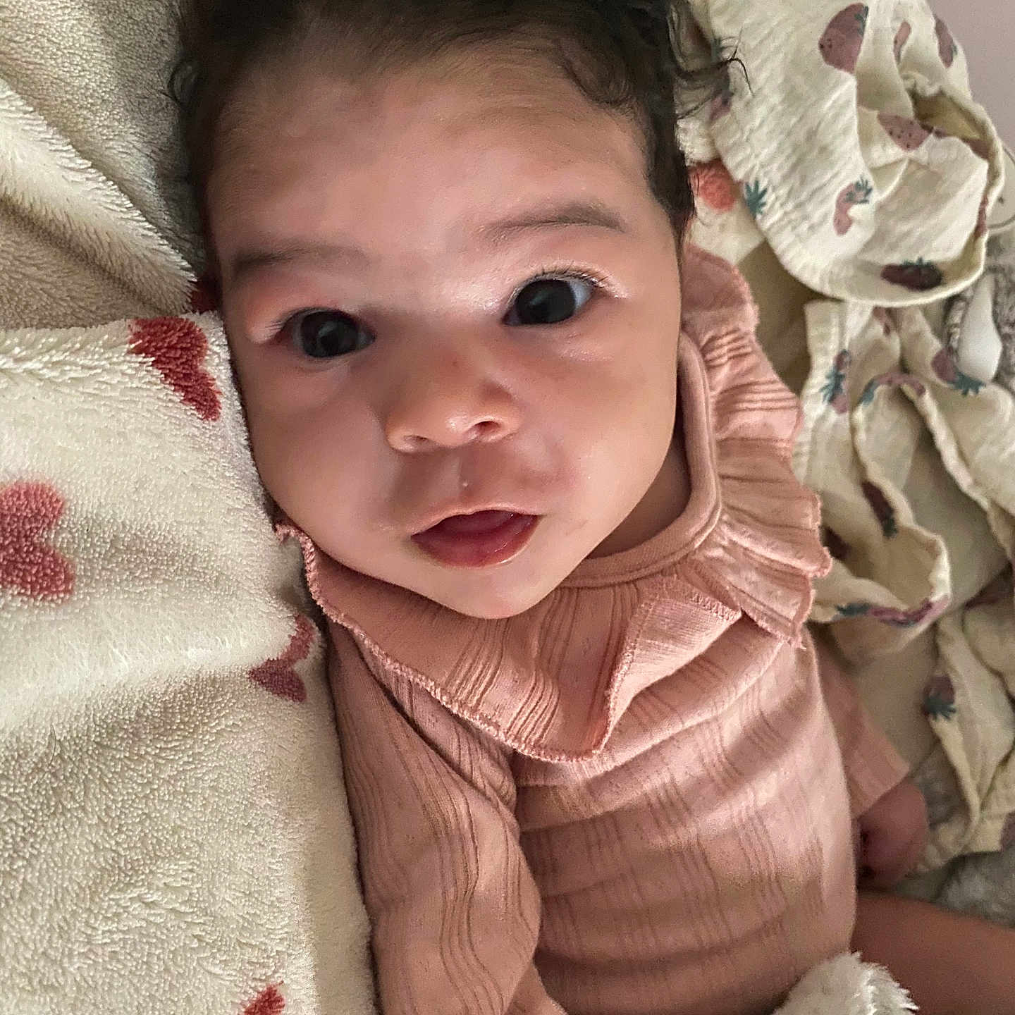 Perla a rejoint le concours — aidez-le/la à gagner de superbes lots ! baby, blanket, child, cozy, curious, cute, eyes, face, fingertip, heart_pattern, indoors, infant, lying_down, pink_clothing, portrait, skin, soft_texture, strawberry_pattern, warm_colors, young_child