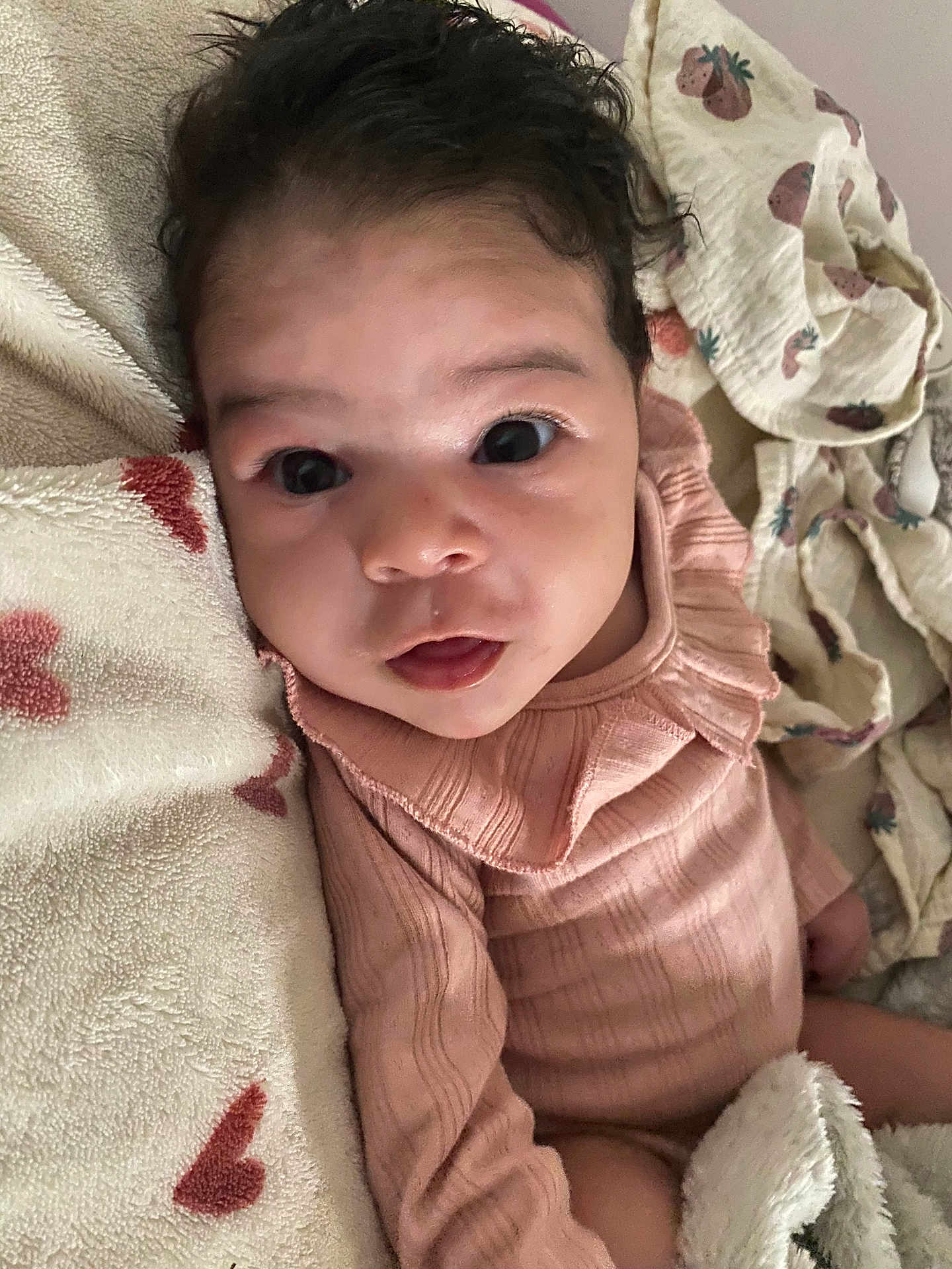 Perla a rejoint le concours — aidez-le/la à gagner de superbes lots ! baby, blanket, child, cozy, curious, cute, eyes, face, fingertip, heart_pattern, indoors, infant, lying_down, pink_clothing, portrait, skin, soft_texture, strawberry_pattern, warm_colors, young_child