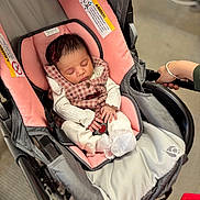 Lydia joined the competition — help win amazing prizes! baby, sleeping, stroller, infant, portrait, indoors, pink, carriage, clothing, checked_pattern, blanket, cushion, hand, adult, parent, peaceful, nap, seated, safety_label, wheelchair_like_stroller