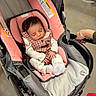 baby, sleeping, stroller, infant, portrait, indoors, pink, carriage, clothing, checked_pattern, blanket, cushion, hand, adult, parent, peaceful, nap, seated, safety_label, wheelchair_like_stroller