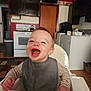 Myles is registered to the contest to win money with this photo: toddler, child, high_chair, bib, smiling, laughing, indoor, kitchen, stove, appliance, cabinet, washing_machine, wooden_floor, striped_clothing, happy, person, home, furniture, baby, young_child