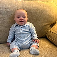 Oakley joined the competition — help win amazing prizes! baby, infant, smile, blue_clothing, knitted_outfit, socks, couch, beige, texture, seated, happy, child, home_interior, portrait, cute, small_hands, small_feet, indoor, warm_lighting, cozy