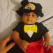 Charlie is registered to the contest to win money with this photo: baby, baby_clothes, baby_fashion, baby_hat, bed, black_shirt, blanket, child, clothing, cute, hand, human, indoors, infant, mickey_mouse_hat, person, portrait, red_shorts, smiling, yellow_bow_tie