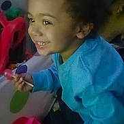 Charlie joined the competition — help win amazing prizes! blue_shirt, carpet, child, closeup, colorful, curly_hair, eyes, face, happy, indoor, lollipop, plastic_toy, playroom, portrait, sitting, smiling, table, teeth, toddler, toy