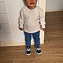 Kaïss a rejoint le concours — aidez-le/la à gagner de superbes lots ! child, boy, standing, smiling, sneakers, jeans, sweater, indoor, wooden_floor, wall, doorway, happy, cute, casual_clothing, portrait, small_person, short_hair, playful, expression, home