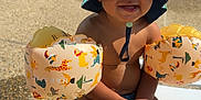 Kaïss a rejoint le concours — aidez-le/la à gagner de superbes lots ! child, toddler, swimwear, bucket_hat, inflatable_arm_floaties, water_park, splash_pad, outdoor, sunny, playful, water, smiling, sitting, lounge_chair, vacation, summer, fun, family, recreation, park