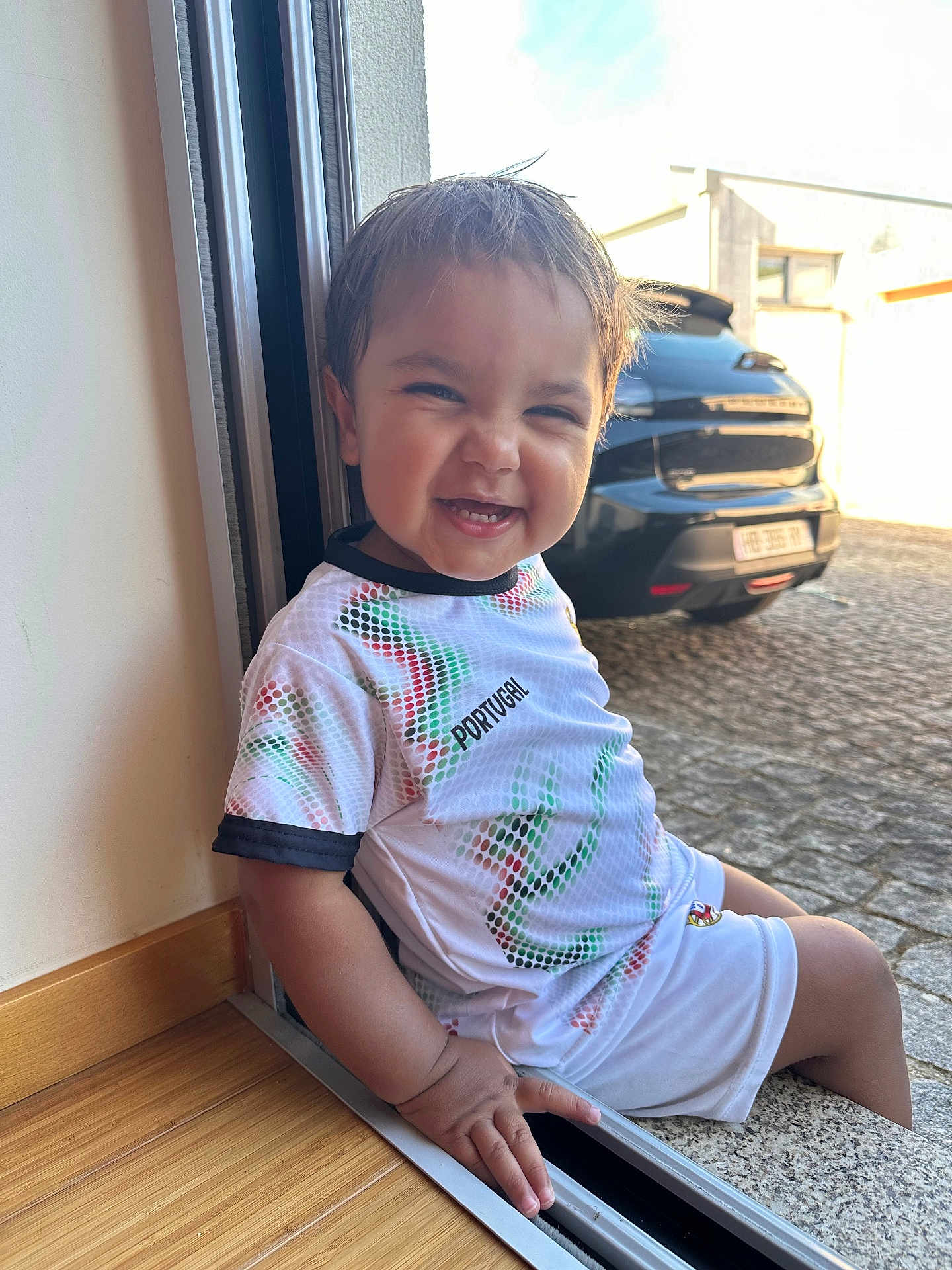 Kaïss a rejoint le concours — aidez-le/la à gagner de superbes lots ! child, toddler, smiling, sitting, doorway, window, shirt, shorts, hand, car, outdoor, pavement, sunlight, happy, face, clothing, person, casual, daylight, home