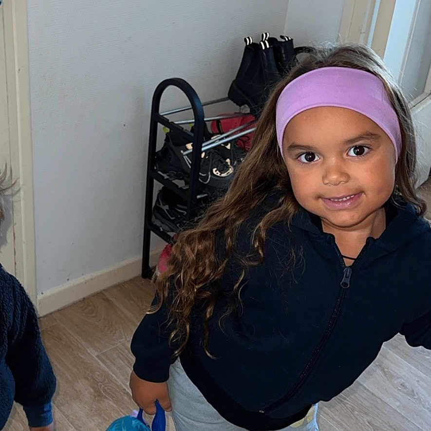 Lahïna a rejoint le concours — aidez-le/la à gagner de superbes lots ! backpack, blue_backpack, boots, cartoon_character, casual_clothing, child, happy, headband, indoor, long_hair, pants, person, playful, purple_headband, shoe_rack, shoes, smiling, standing, wooden_floor, young_child