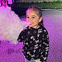 child, girl, cotton_candy, food, night, street, pavement, smiling, happy, casual_clothing, sneakers, long_hair, outdoor, fence, grass, purple_light, cute, playful, portrait, sweet_treat
