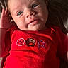 baby, infant, red_clothing, face, hand, eyes, smile, lying_down, fabric, pattern, portrait, cute, child, sleepwear, newborn, human, skin, expression, indoors, soft_light
