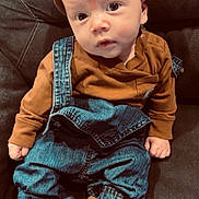 Stetson is registered to the contest to win money with this photo: baby, infant, beanie, brown_clothing, denim_overalls, plush_slippers, animal_slippers, couch, indoor, child, cute, casual_wear, portrait, seated, soft_lighting, cozy, small_hands, face, footwear, fashion