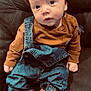 baby, infant, beanie, brown_clothing, denim_overalls, plush_slippers, animal_slippers, couch, indoor, child, cute, casual_wear, portrait, seated, soft_lighting, cozy, small_hands, face, footwear, fashion