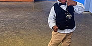Gabriel a rejoint le concours — aidez-le/la à gagner de superbes lots ! toddler, child, smiling, walking, indoor, vest, bow_tie, khaki_pants, sneakers, floor, wall, bench, happy, playful, person, young_child, black_hair, concrete_floor, casual, cute