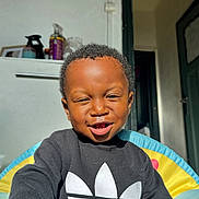 Gabriel a rejoint le concours — aidez-le/la à gagner de superbes lots ! adidas_logo, black_sweatshirt, casual_clothing, chair, child, colorful, container, door, face, hand, happy, indoor, portrait, room, short_hair, sitting, smiling, sunlight, toddler, toy