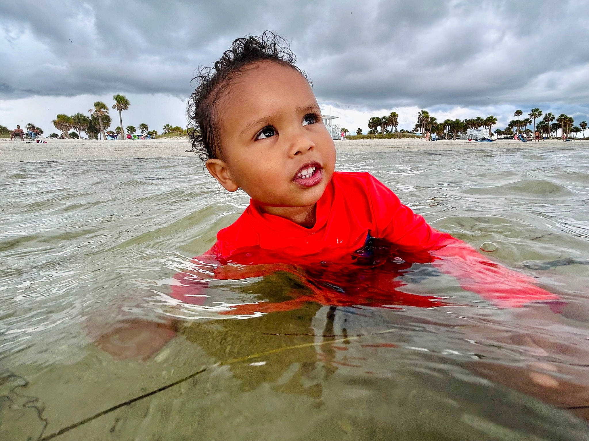 Emi is registered to the contest to win money with this photo: bathing, beach, body_of_water, child, cloud, fun, happy, lake, leisure, ocean, outdoor_recreation, people_in_nature, people_on_beach, person, personal_protective_equipment, recreation, sky, toddler, water, wave