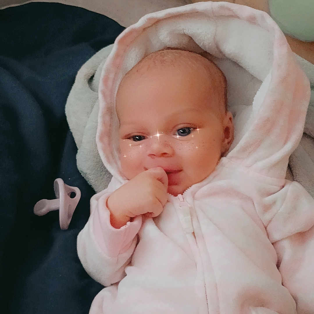 Zanayah is registered to the contest to win money with this photo: baby, blanket, child, comfort, cute, expression, face, hand, head, hood, indoors, infant, lying_down, pacifier, pink_onesie, portrait, skin, sleepwear, soft_lighting, sparkle_filter