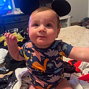 Timothy joined the competition — help win amazing prizes! baby, child, infant, sitting, smiling, face, portrait, indoors, bedroom, bed, laundry, clothing, dinosaur_print, mouse_ears, toy_headband, television, furniture, home, happy, casual_photo