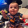 baby, child, infant, sitting, smiling, face, portrait, indoors, bedroom, bed, laundry, clothing, dinosaur_print, mouse_ears, toy_headband, television, furniture, home, happy, casual_photo