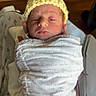 newborn, baby, infant, sleeping, hospital, bassinet, yellow_hat, knitted_cap, swaddled, blanket, face, portrait, indoors, medical_equipment, monitoring_wires, wood_floor, resting, tiny, peaceful, photography