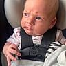 baby, infant, child, car_seat, harness, portrait, sitting, serious_expression, blue_eyes, blond_hair, rosy_cheeks, blanket, striped_blanket, indoor, close_up, face, hand, clothing, safety_buckle, photography