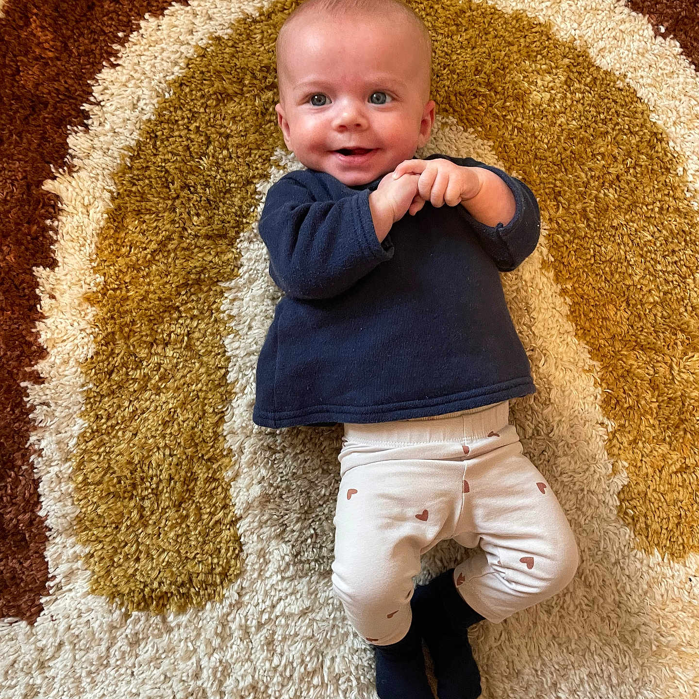 Lou participe au concours pour gagner de l'argent avec cette photo : baby, blue_top, child, clothing, cozy, cute, floor, happy, heart_pattern, indoor, infant, laying_down, pattern, portrait, rug, small_hands, smiling, socks, warm_colors, white_leggings