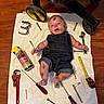 Steven is registered to the contest to win money with this photo: baby, denim_overalls, tools, screwdriver, wrench, tape_measure, lubricant_can, towel, wood_floor, smiling, face_paint, dirty_spots, baby_cart, infant, floor, playful, cute, indoors, child, person