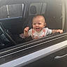 baby, car, child, clothing, cute, door, face, hand, happy, head, interior, joy, overalls, person, seat, smile, steering_wheel, vehicle, window, young