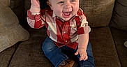 Steven is registered to the contest to win money with this photo: baby, child, cowboy_hat, plaid_shirt, jeans, brown_boots, couch, smiling, happy, indoors, person, sitting, cute, hat, footwear, young, toddler, clothing, furniture, portrait