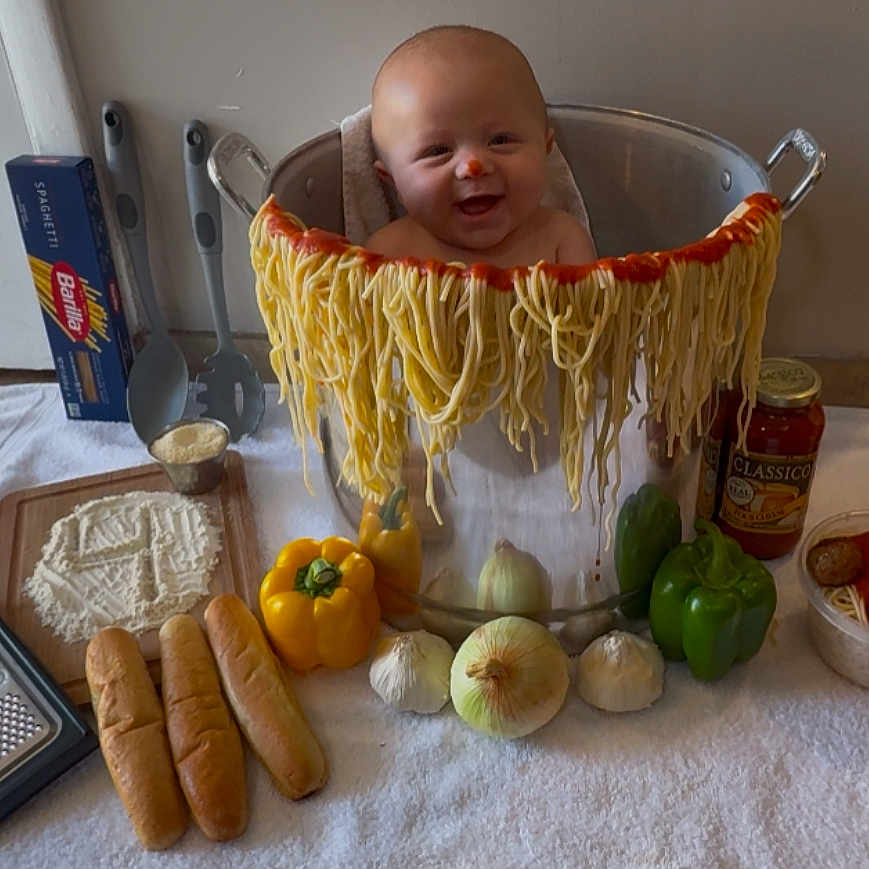 Steven is registered to the contest to win money with this photo: baby, child, spaghetti, noodles, pot, kitchen, food, bread, yellow_bell_pepper, green_bell_pepper, onion, garlic, pasta_sauce, meatballs, grater, cutting_board, towel, smiling, indoor, cooking