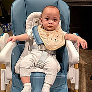 Wesley Joeward is registered to the contest to win money with this photo: baby, high_chair, bib, baby_clothes, socks, indoor, floor_tiles, furniture, child, person, seat_belt, modern_chair, home, kitchen, neutral_expression, cute, infant, white_clothing, blue_chair, toddler