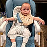 baby, high_chair, bib, baby_clothes, socks, indoor, floor_tiles, furniture, child, person, seat_belt, modern_chair, home, kitchen, neutral_expression, cute, infant, white_clothing, blue_chair, toddler