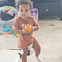 toddler, child, indoor, carpet, toy, orange_ball, brown_shirt, diaper, white_sock, furniture, living_room, curly_hair, person, playtime, cute, standing, carpeted_floor, plastic_toy, baby_chair, candid