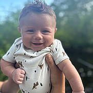 Elijah is registered to the contest to win money with this photo: baby, smiling, infant, onesie, clothing, human_hand, outdoor, nature, portrait, cute, happy, child, person, skin, face, young, holding, human_arm, daylight, expression