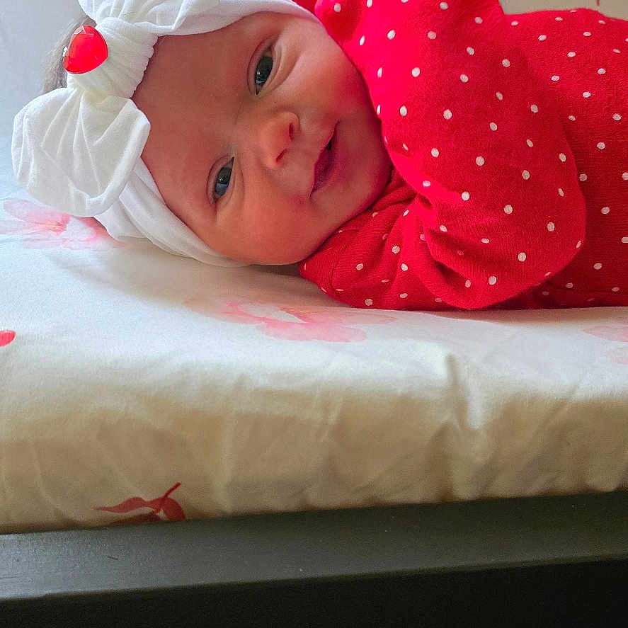 Daizlynn is registered to the contest to win money with this photo: adorable, baby, bed, blanket, bow, child, cute, face, floral_pattern, headband, indoors, infant, lying_down, person, polka_dots, portrait, red_clothing, smile, soft_light, young