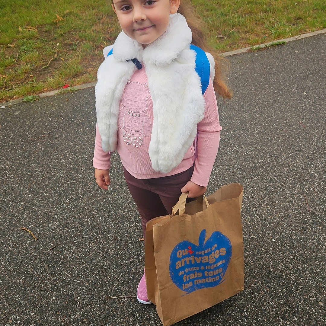 Elsa participe au concours pour gagner de l'argent avec cette photo : backpack, building, casual, child, clothing, daytime, footwear, girl, grass, nature, outdoor, paper_bag, pavement, person, pink_sweater, portrait, sidewalk, smile, trees, white_scarf