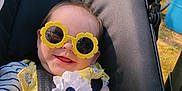 Kovelynn is registered to the contest to win money with this photo: baby, sunglasses, yellow_outfit, flower, smile, stroller, outdoor, sunlight, child, happy, infant, toy, hand, foot, seatbelt, nature, grass, car, person, cute
