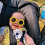 baby, sunglasses, yellow_outfit, flower, smile, stroller, outdoor, sunlight, child, happy, infant, toy, hand, foot, seatbelt, nature, grass, car, person, cute