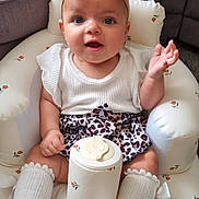 River-Rose is registered to the contest to win money with this photo: baby, child, infant, girl, headband, bow, leopard_print, skirt, socks, cushioned_chair, patterned, white_clothing, sitting, indoor, cute, expression, person, face, legs, small_container