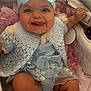 baby, child, blue_bow, headband, crochet_sweater, floral_dress, stroller, pink_blanket, smiling, tongue_out, cute, infant, happy, seated, soft_fabric, closeup, indoors, adorable, person, portrait