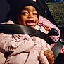 child, toddler, smiling, car_seat, seatbelt, pink_coat, black_hat, red_bow, outdoor, nighttime, happy, person, clothing, baby, cute, warm_clothes, face, hands, sitting, portrait