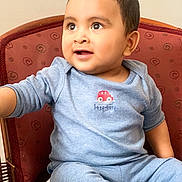 Hyzin is registered to the contest to win money with this photo: toddler, child, baby, blue_pajamas, chair, indoor, curious, smiling, face, cute, seated, patterned_chair, short_hair, small_car_emblem, happy, person, young_child, portrait, cozy, expression