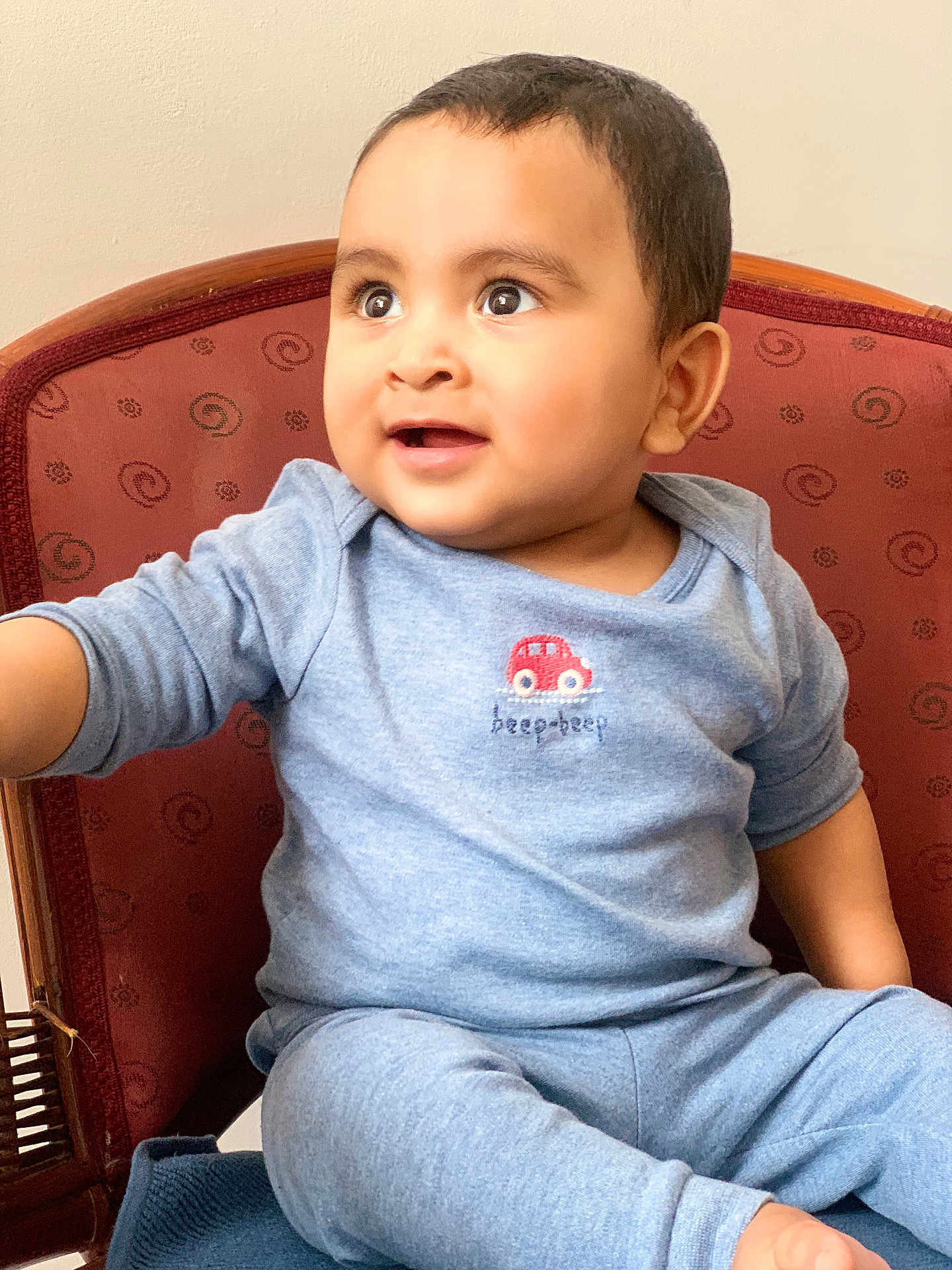 Hyzin is registered to the contest to win money with this photo: toddler, child, baby, blue_pajamas, chair, indoor, curious, smiling, face, cute, seated, patterned_chair, short_hair, small_car_emblem, happy, person, young_child, portrait, cozy, expression