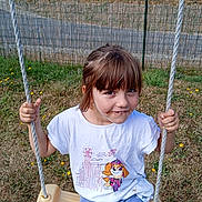 Rose a rejoint le concours — aidez-le/la à gagner de superbes lots ! brown_hair, cartoon_print, casual_clothing, child, daylight, face, fence, fun, grass, happy, holding, nature, outdoor, playground, rope, smiling, swing, white_tshirt, yellow_flowers, young_person